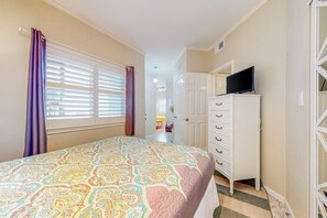 Ein Schlafzimmer mit einem Bett, einem Fernseher auf einer Kommode und einem Fenster mit Jalousien.