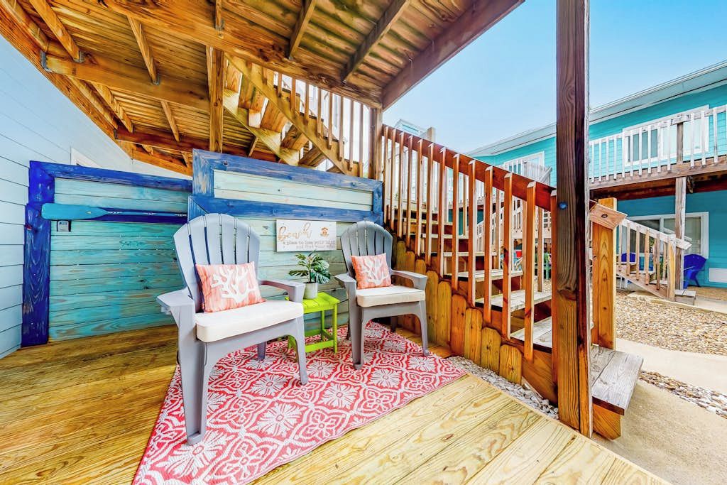 An outdoor seating area with two chairs, a small table, and a red patterned rug.