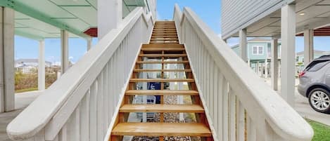 A wooden staircase with white railings leading to a covered area with a car parked nearby.
