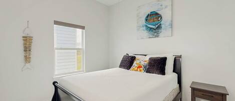 A bedroom with a bed, a bedside table, a window, and a wall-mounted artwork.