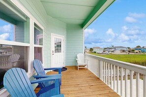 A covered porch with two Adirondack chairs, a white door, and a view of a residential area. - Salty Soles - Shared Pool, Patio & BBQ (Rockport)