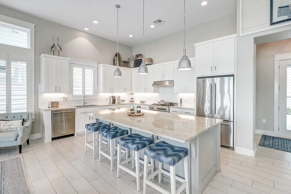 A modern kitchen with white cabinetry, a large island with bar stools, stainless steel appliances, pendant lighting, and a view of the adjacent living area.