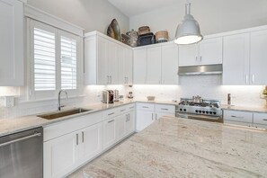 A modern kitchen with white cabinetry, a stainless steel dishwasher, a built-in stove, and a large island with a marble countertop. - Waterfront Paradise | Private Pool & Dock, Poolside TV & Multi-TV Game Room (Rockport)