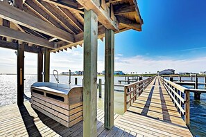 A wooden pier extending into calm waters, with a covered seating area and a view of distant buildings. - Waterfront Paradise | Private Pool & Dock, Poolside TV & Multi-TV Game Room (Rockport)