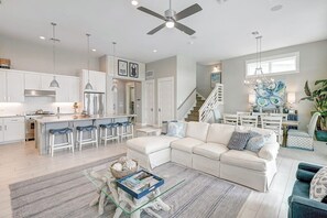 A modern kitchen with white cabinetry, a dining area with a white table and chairs, a living room with a white sofa and blue cushions, and a staircase leading to another level. - Waterfront Paradise | Private Pool & Dock, Poolside TV & Multi-TV Game Room (Rockport)