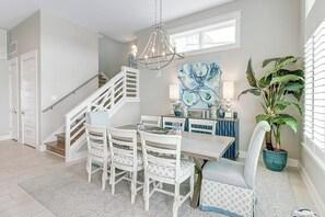 A dining area with a staircase, a chandelier, a painting, and a potted plant. - Waterfront Paradise | Private Pool & Dock, Poolside TV & Multi-TV Game Room (Rockport)
