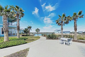 A pathway leading to a white table and chairs, surrounded by palm trees and a clear blue sky. - Waterfront Paradise | Private Pool & Dock, Poolside TV & Multi-TV Game Room (Rockport)