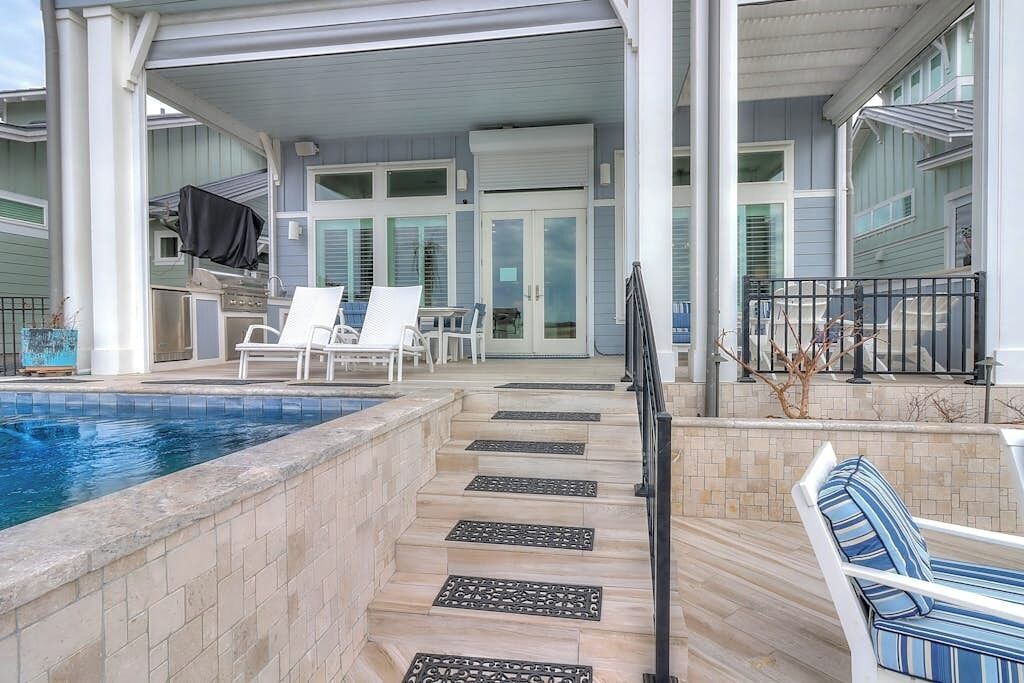 Espaço coberto ao ar livre com piscina, espreguiçadeiras e churrasqueira.