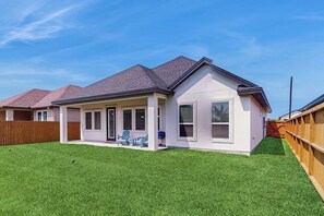 Ein Wohnhaus mit überdachter Terrasse, einem umzäunten Garten und einem gepflegten Rasen.