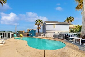 Ein Swimmingpool mit Liegestühlen und einem eingezäunten Bereich, umgeben von Palmen und einem Gebäude.
