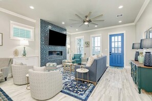 Ein geräumiges Wohnzimmer mit blauer Tür, Kamin und Deckenventilator.