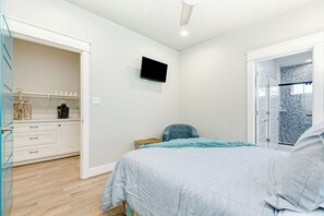 Une chambre à coucher avec un lit, un téléviseur fixé au mur et une armoire dont les portes sont ouvertes.