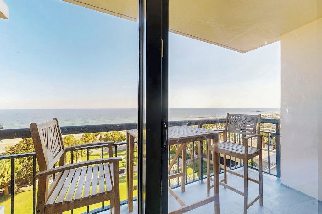 A balcony with two wooden chairs and a table, overlooking a body of water.