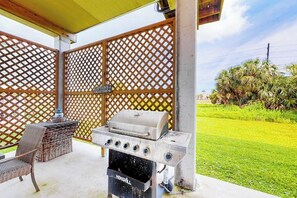 An outdoor grill area with a wooden fence, a grill, and wicker furniture. - Captain's Quarters - Walk to the Beach, Patio (Galveston)