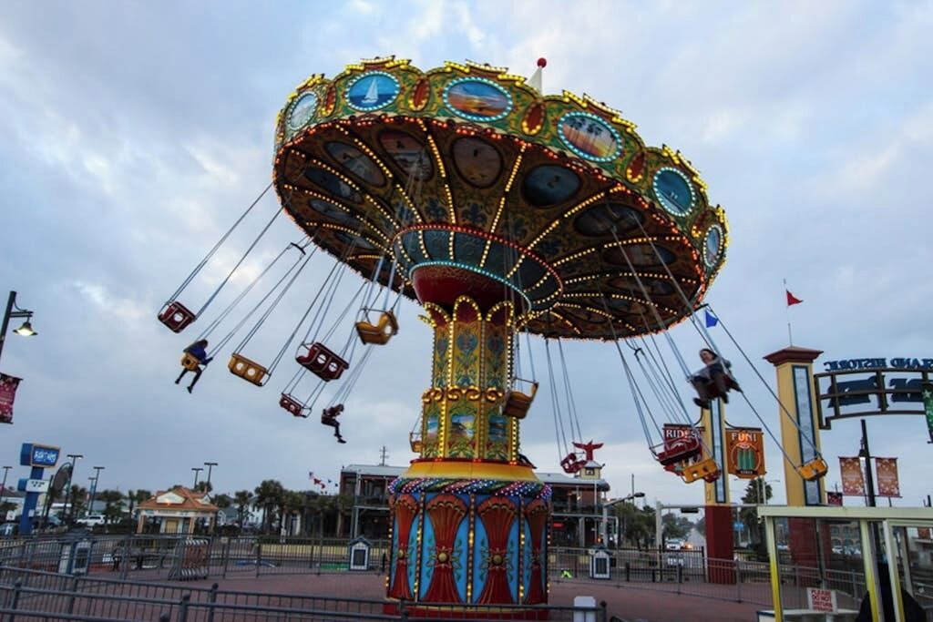 A carousel with multiple seats and a central pole, surrounded by a fenced area.