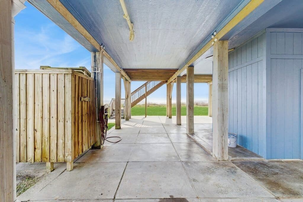 An open covered area with a concrete floor, wooden posts, and a metal staircase leading to an upper level.