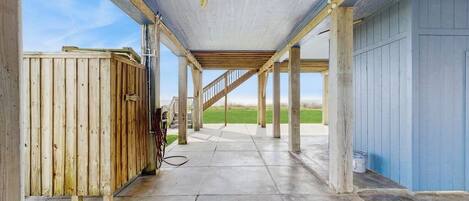 An open covered area with a concrete floor, wooden posts, and a metal staircase leading to an upper level.