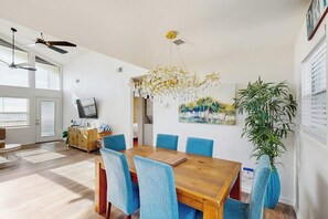 Uma sala de jantar com uma mesa de madeira e cadeiras azuis, um candelabro e um quadro na parede.