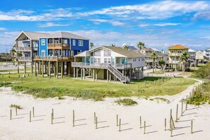Ein Anwesen direkt am Strand mit mehreren Häusern auf Stelzen, mit Balkonen und einem Sandstrand im Vordergrund.