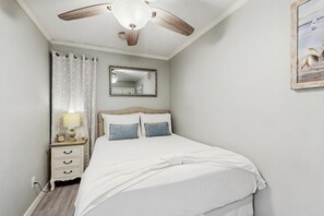 Une chambre à coucher avec un lit, un ventilateur de plafond, une table de chevet, un miroir et un tableau accroché au mur.