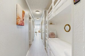 A narrow hallway with a bed on the right, a painting on the left, and a circular mirror on the wall. - Sun of a Beach - Gulf-Front, Pools, Steps to Sand (Galveston)