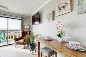A dining area with a wooden table, chairs, a potted plant, and a television on the wall. - Sun of a Beach - Gulf-Front, Pools, Steps to Sand (Galveston)