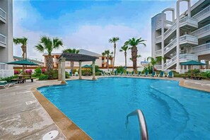 A swimming pool with lounge chairs and palm trees. - Sun of a Beach - Gulf-Front, Pools, Steps to Sand (Galveston)