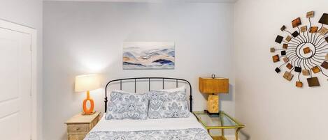 A bedroom with a bed, two bedside tables, a wall art piece, and a decorative wall hanging.