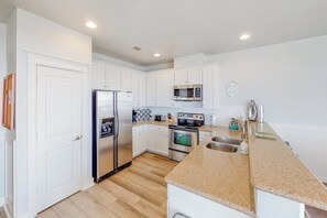A modern kitchen with white cabinetry, stainless steel appliances, and a granite countertop. - Pointe West Resort - 203 (Galveston)