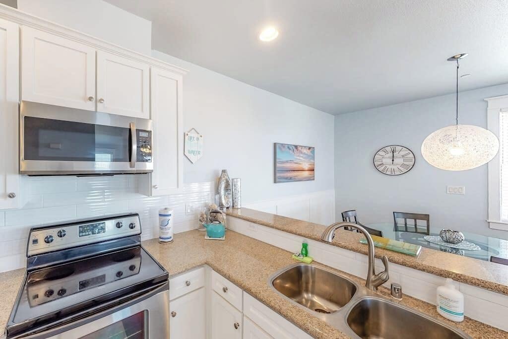 A kitchen with white cabinets, stainless steel appliances, a granite countertop, a double sink, and a pendant light.