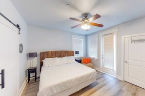 Ein Schlafzimmer mit einem Bett, Deckenventilator, Nachttisch, Lampe und einem Fenster mit Jalousien.