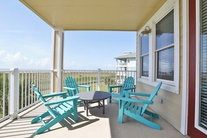 A covered outdoor seating area with a table and chairs, overlooking a view of the ocean and a building. - Pointe West Resort - 203 (Galveston)