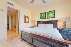 Ein Schlafzimmer mit einem großen Bett, zwei Nachttischen, einem Beistelltisch, einem Deckenventilator und Kunstwerken an der Wand.