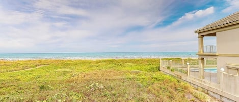Une propriété située en bord de mer, offrant une vue sur l’océan, avec une zone herbeuse et un bâtiment doté d’un balcon.