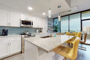 A modern kitchen with white cabinets, a stainless steel microwave, and a large island with a sink. - Sunchase IV #311 - 2 Balconies & Heated Pools (South Padre Island)