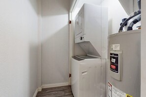 A compact, white utility room with a built-in washer and dryer, a visible water pipe, and a warning label on the dryer. - Sunchase IV #311 - 2 Balconies & Heated Pools (South Padre Island)