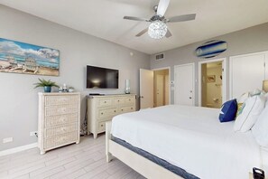 Une chambre à coucher avec un lit, un ventilateur de plafond, une télévision, une commode et un tableau accroché au mur.