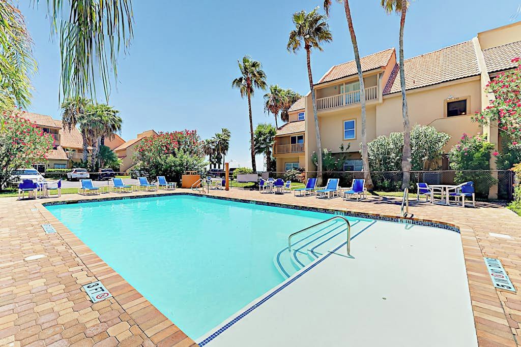 Ein Swimmingpool mit gefliestem Deck, umgeben von Liegestühlen und Palmen.