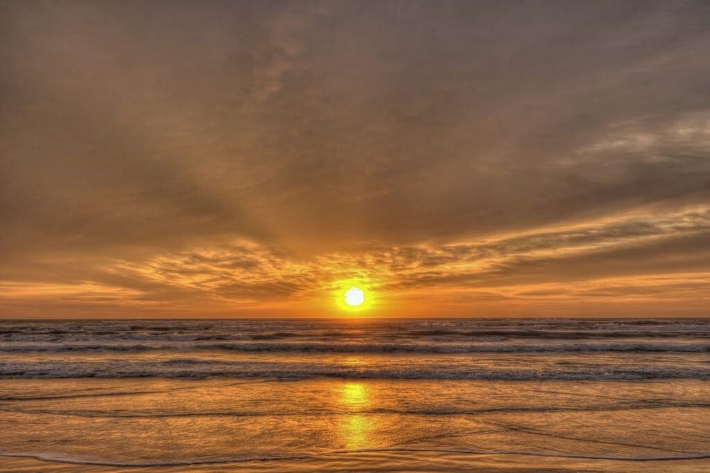Een zonsondergang boven de oceaan, met golven die de hemel weerspiegelen.