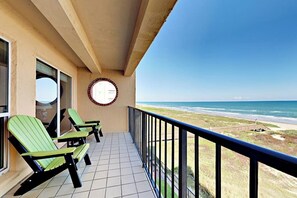 A balcony with two green chairs, a tiled floor, and a view of the beach and ocean. - Suntide II Condominiums #402 (South Padre Island)
