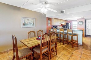 A dining area with a wooden table and chairs, a ceiling fan, and a kitchen in the background. - Suntide II Condominiums #402 (South Padre Island)