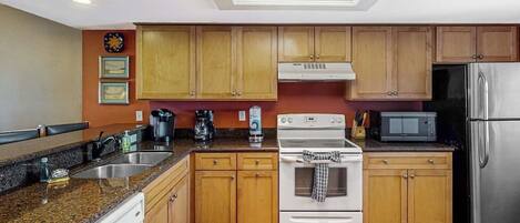 A kitchen with wooden cabinets, a stainless steel refrigerator, a microwave, and a stove.