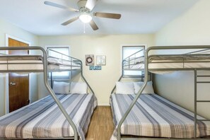 A room with bunk beds, a ceiling fan, and a door. - Mezquite Duplex Beach House A (South Padre Island)