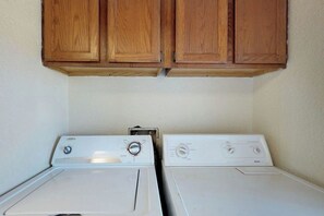 A laundry room with two white washing machines and wooden cabinets above. - Mezquite Duplex Beach House A (South Padre Island)