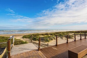 Ein hölzerner Steg führt zu einem Strand unter blauem Himmel.