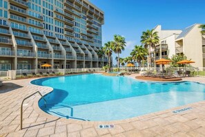 A swimming pool with a 9-inch depth marker, surrounded by lounge chairs and umbrellas, with a high-rise building in the background. - Solare Garden Villa 771F (South Padre Island)