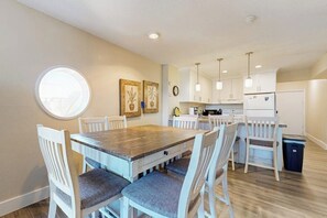 A dining area with a wooden table and white chairs, a kitchen with white cabinets, and a round window. - Solare Garden Villa 771F (South Padre Island)
