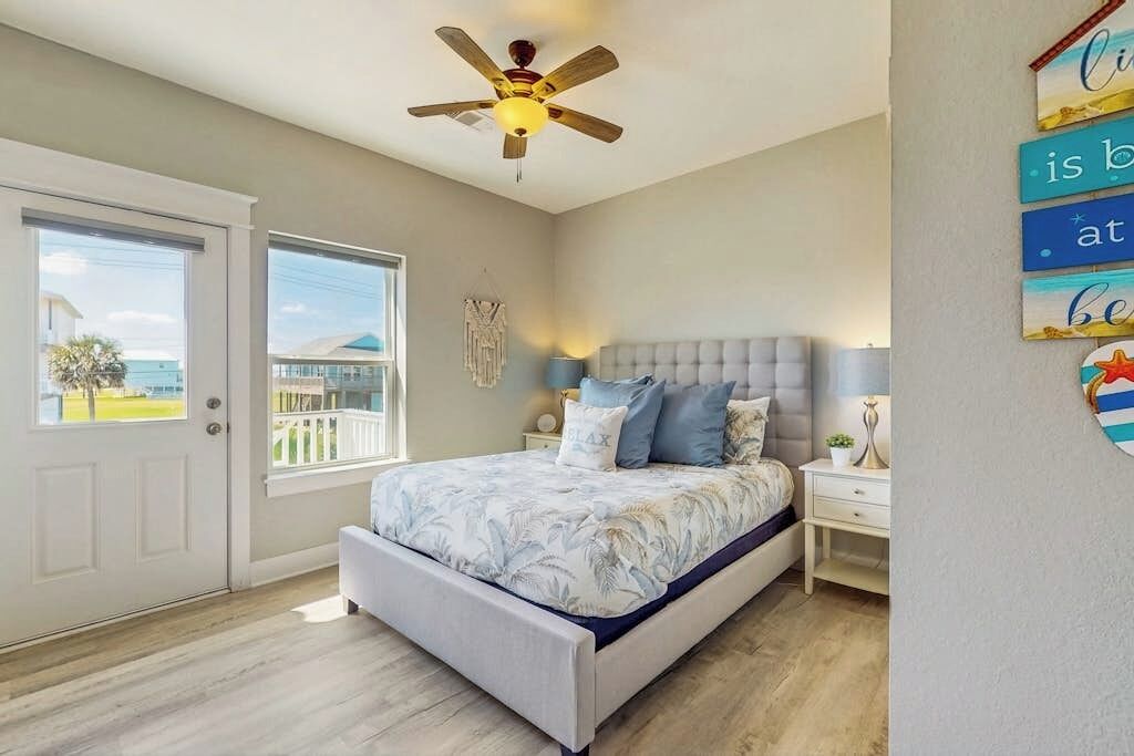 A bedroom with a bed, a ceiling fan, a nightstand, and a window with a view.