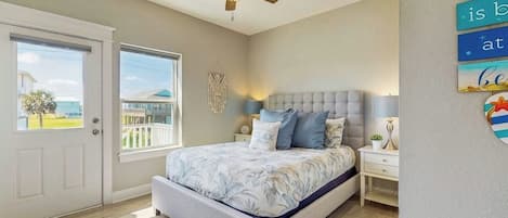 Quarto com cama, ventilador de teto, mesa de cabeceira e janela com vista.