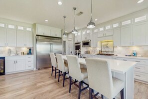 Una cocina moderna con muebles blancos, electrodomésticos de acero inoxidable e iluminación colgante.